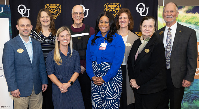 A group of people smiling in front of an OU background