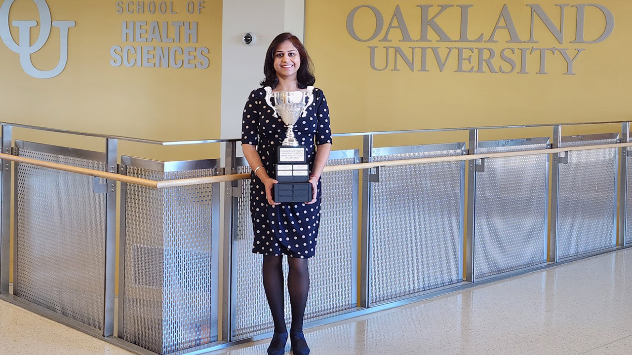 Woman stands in O U building holding a trophy.