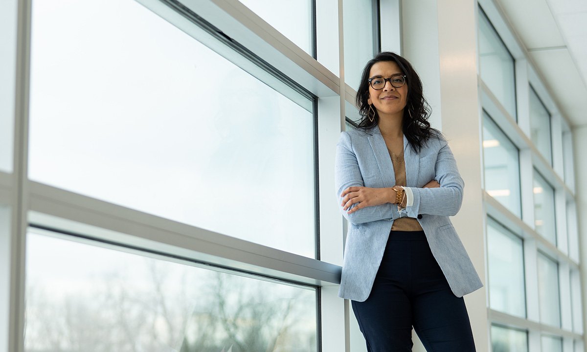 Woman standing in front of bank of windows, smiling, arms crossed.