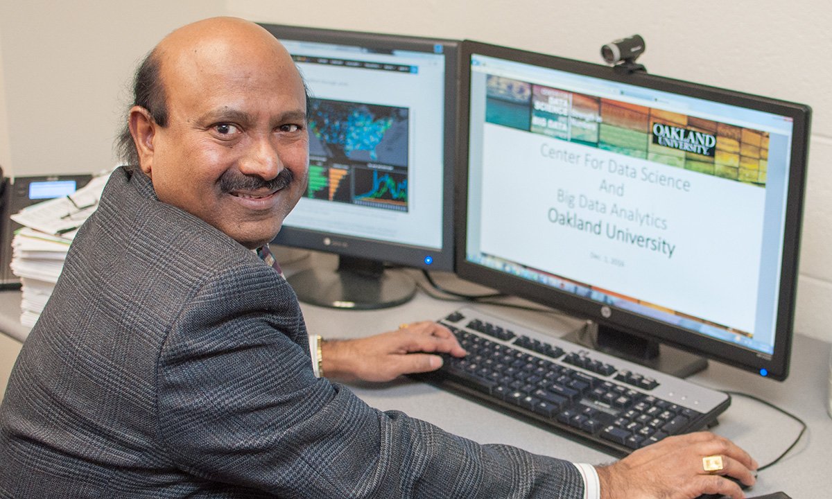 Man working on computer, turns from desk toward camera.