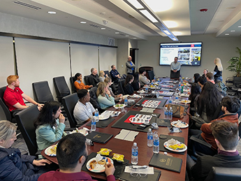 People sitting at a large conference table looking at a person presenting with a screen