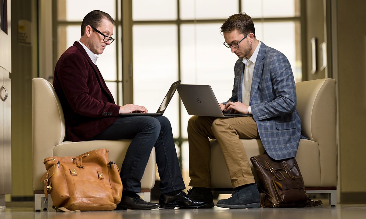 Two men sitting in chairs working on computers.