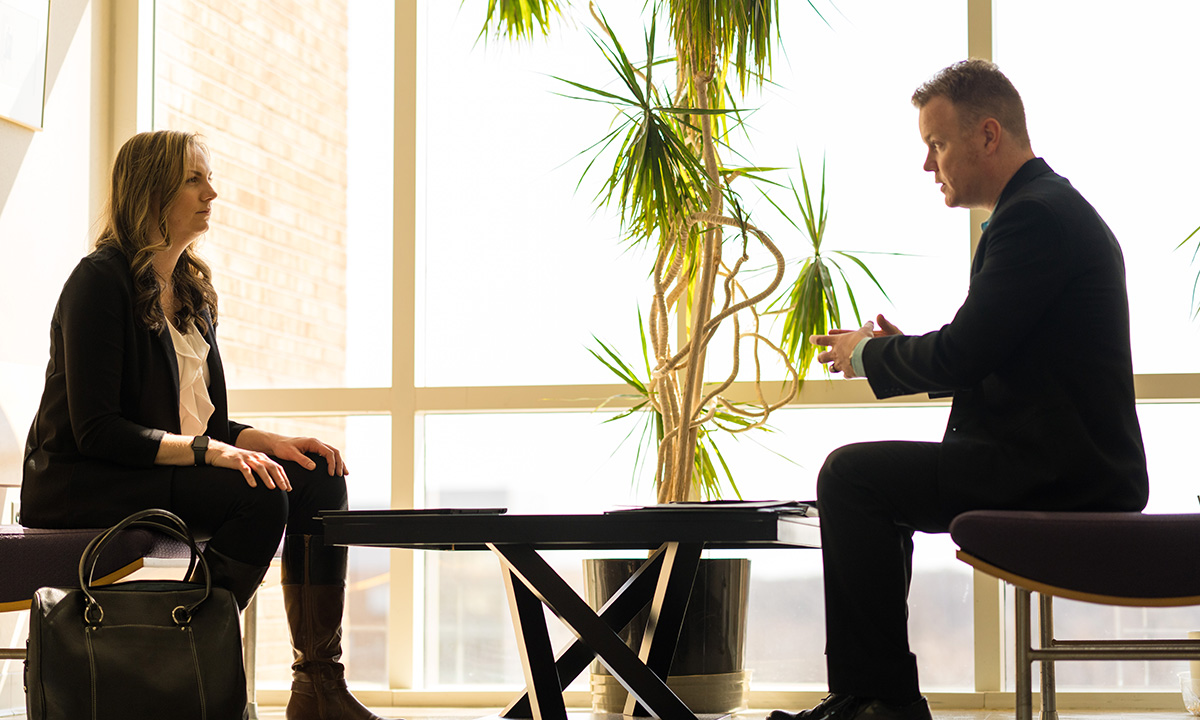 A man and woman sitting across from one another at a table in a lobby.