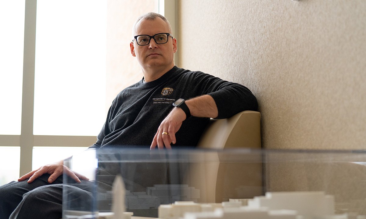 Man wearing glasses sitting in chair looking toward camera.