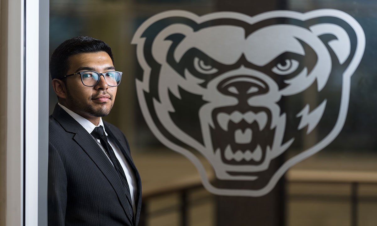 A man posing with a grizzhead in the background.