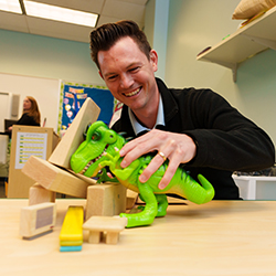 A man playing with a toy dinosaur.