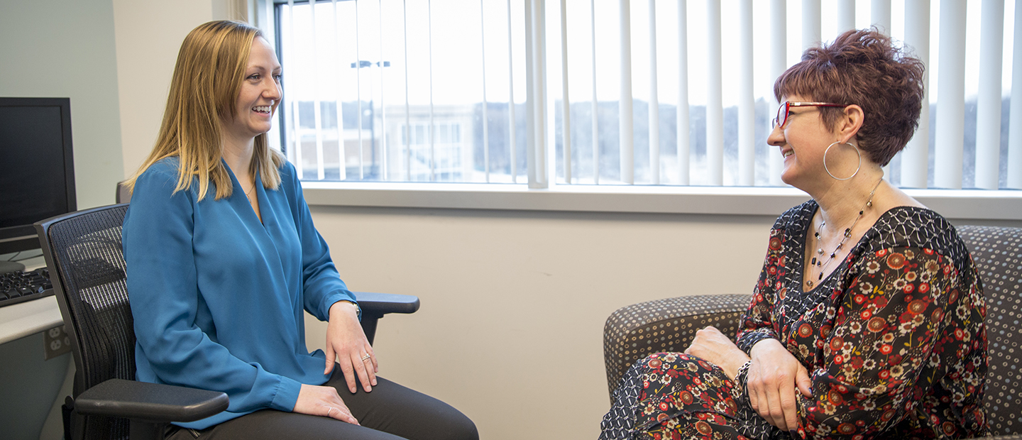 Two women seated in office chairs facing each other, smiling.
