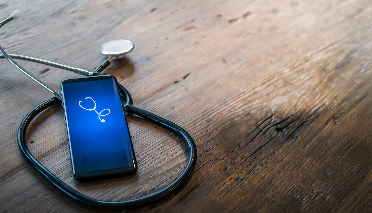 wooden table with a stethoscope and smart phone on top