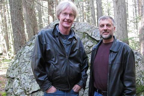Two men standing outside with trees in the background.