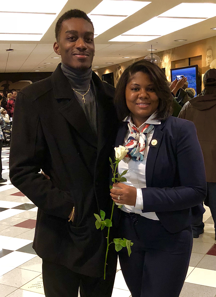 A couple posing for a photo, with the woman on the right holding a rose