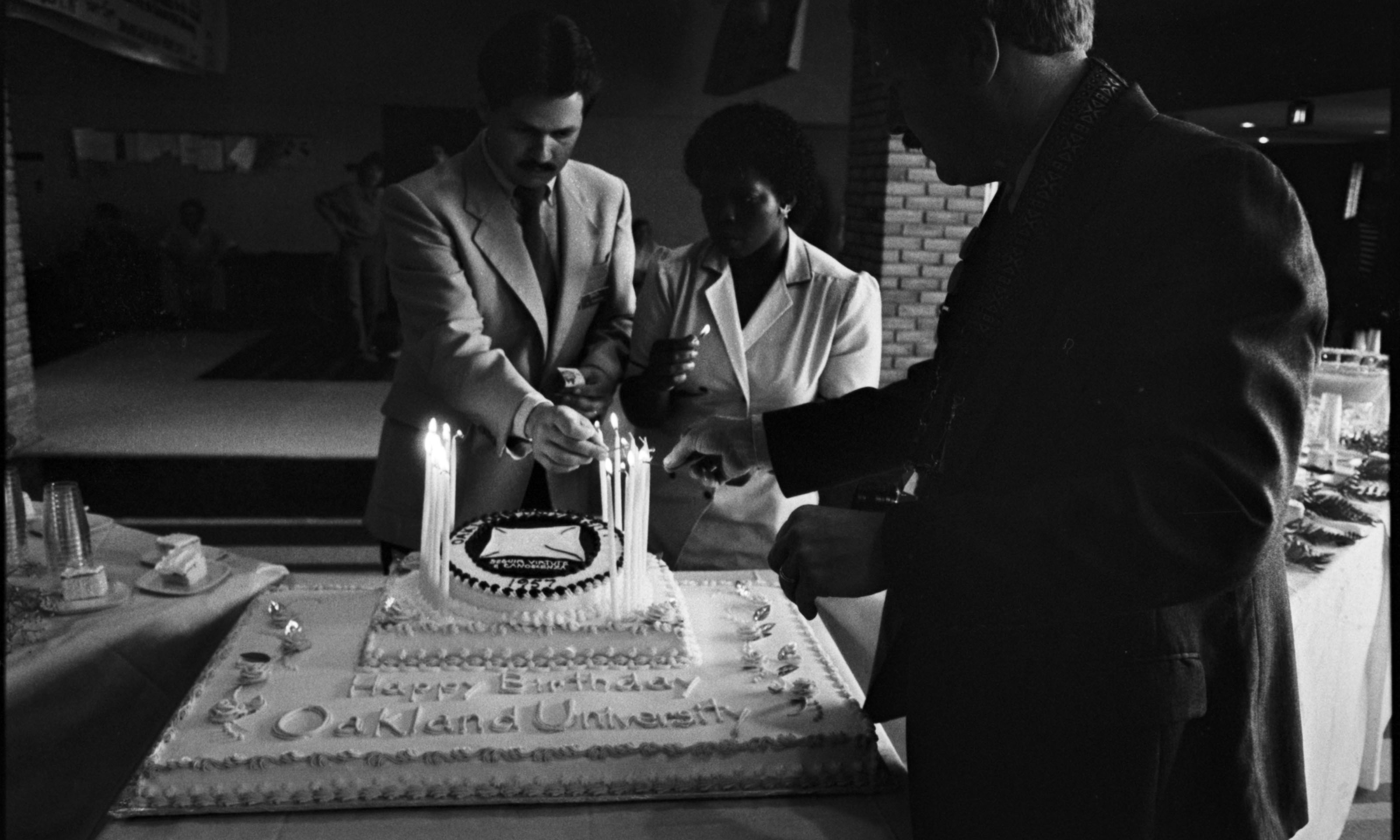 A black and white photo of people cutting a cake