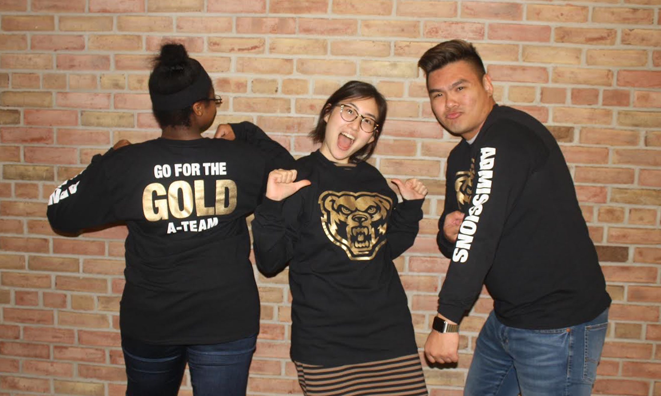 Three students in front of a brick wall wearing 
