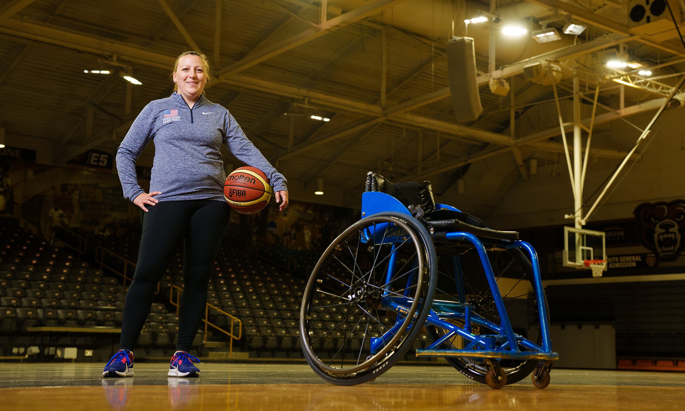 A person on a basketball court standing next to a wheelchair and holding a basketball