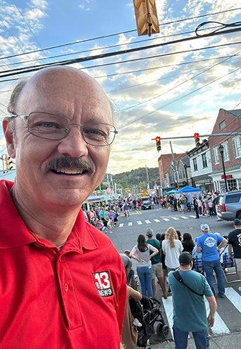 Person taking a selfie with a crowd of people behind him on the street