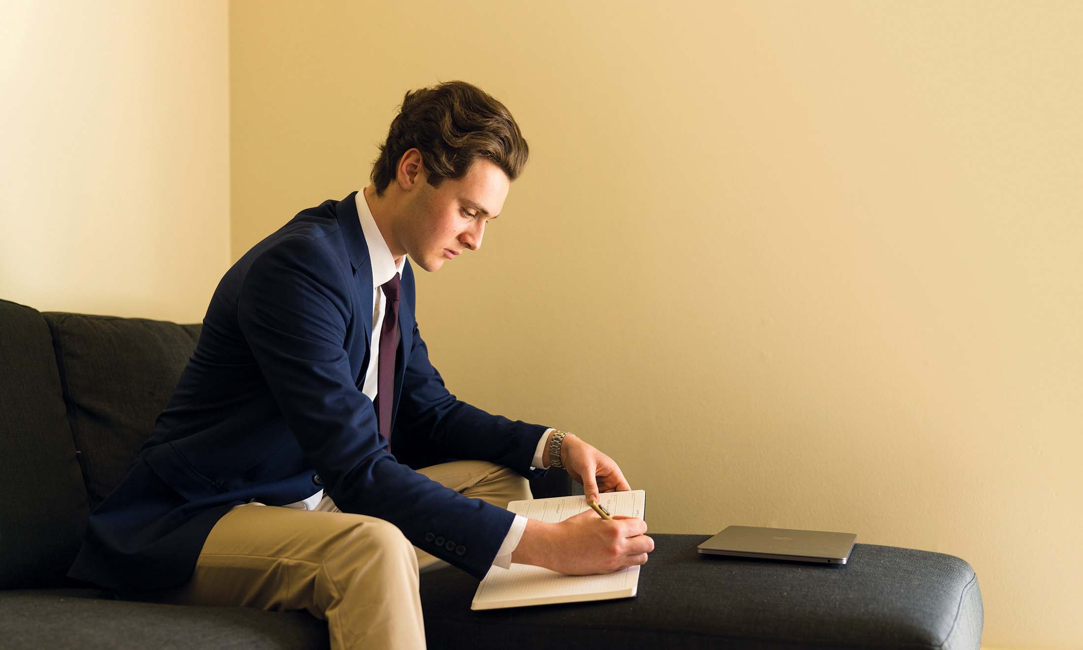 Male student sitting on chair writing in notebook