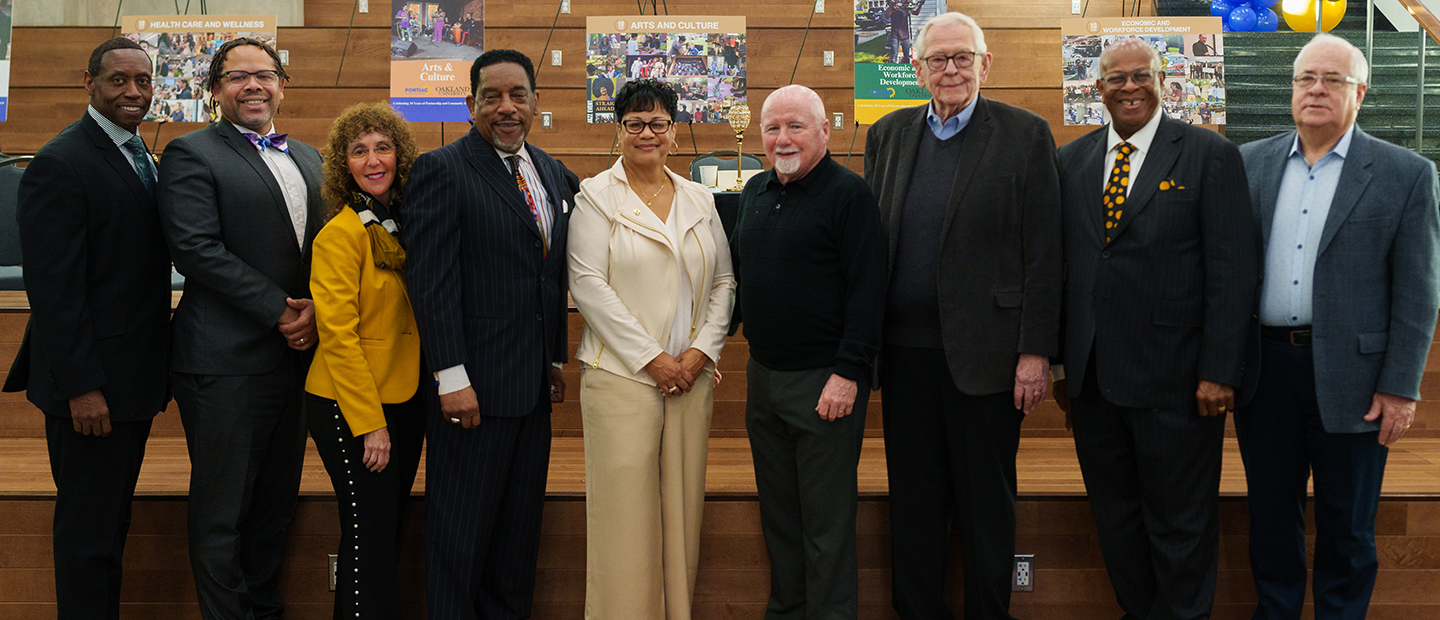 Seven men and two women standing facing the camera in front of a bunch of posters and easels.