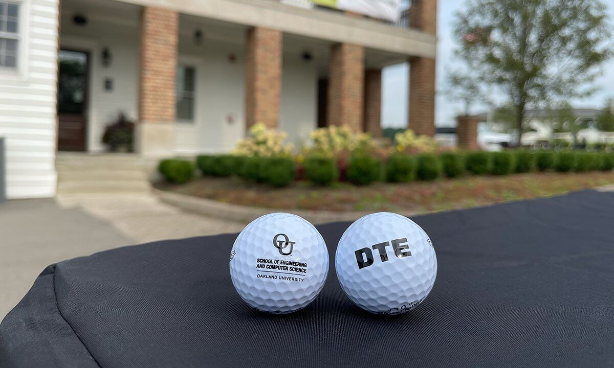 Two golf balls on a table, one reads OU School of Engineering and Computer Sciences Oakland University the other DTE