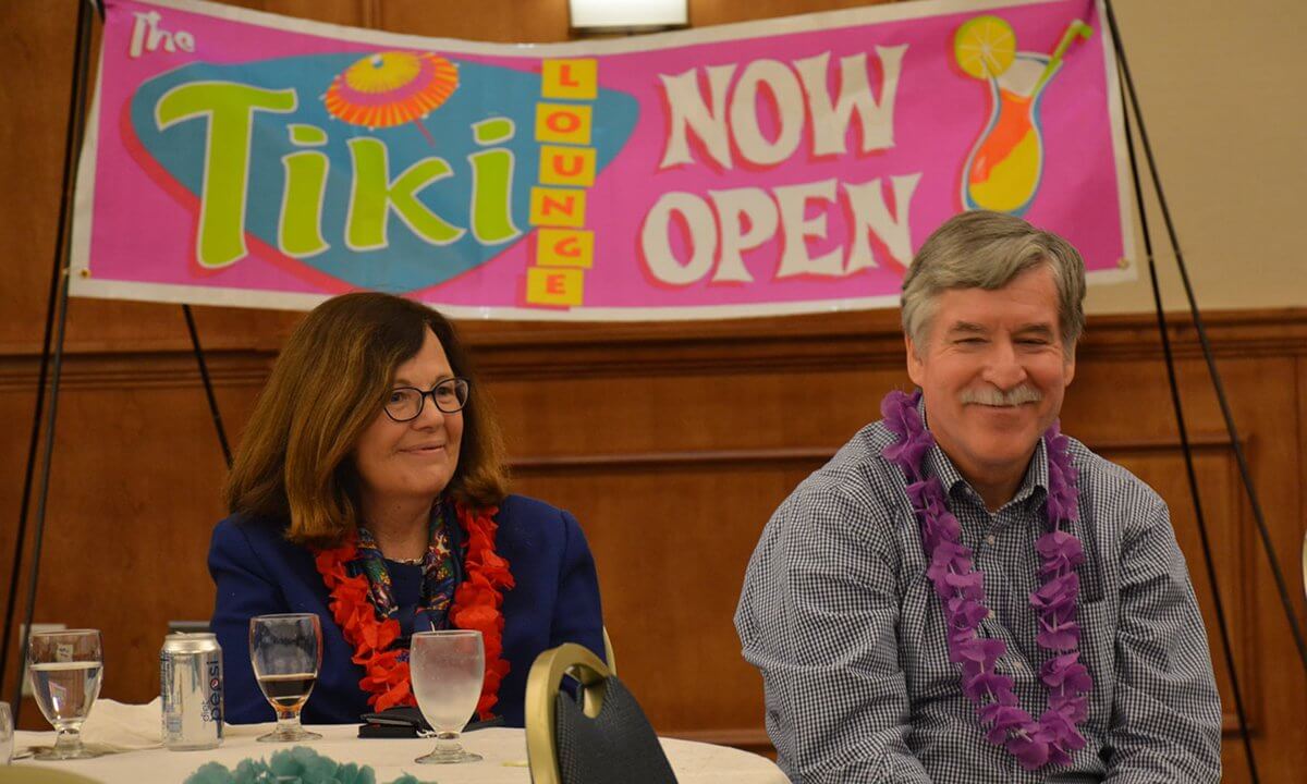 A man and a woman sitting at the table. They are wearing Hawaiian leis.