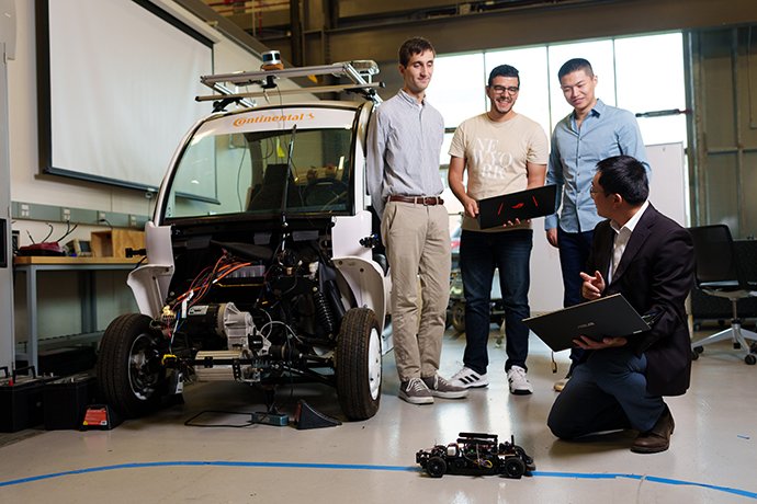 Four people working in a lab next to a vehicle