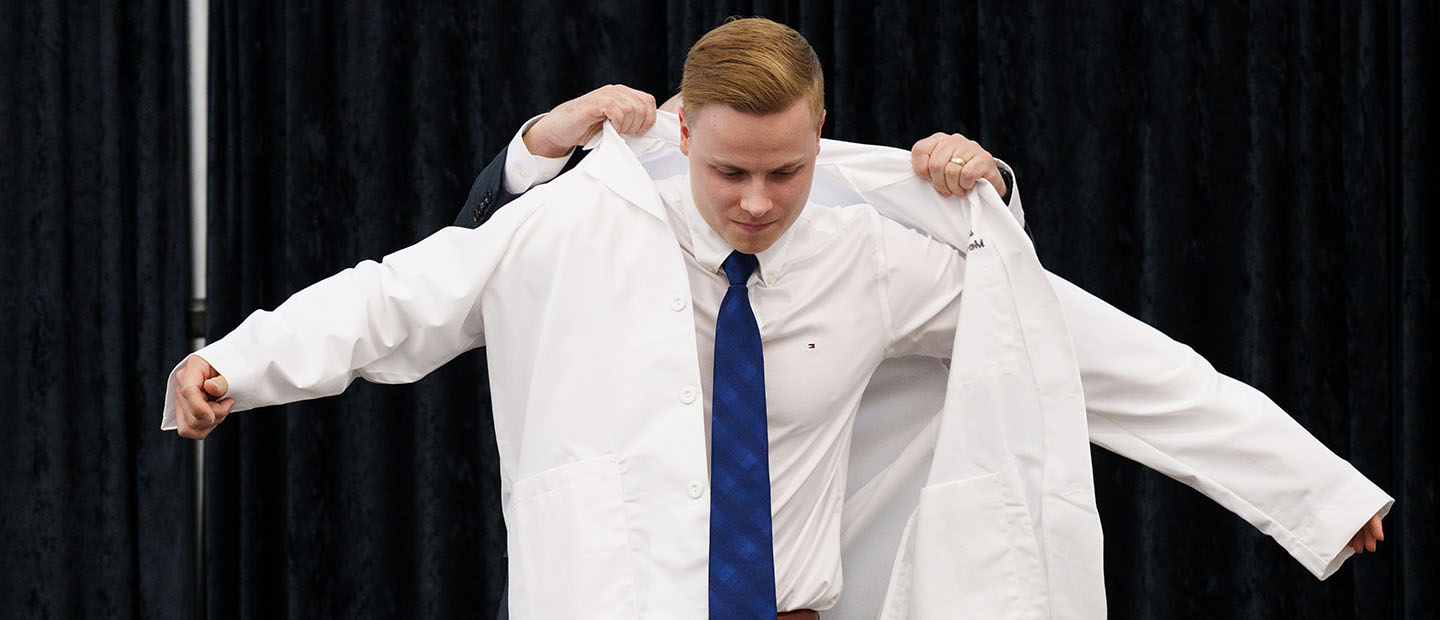 A man putting on a white doctor's coat