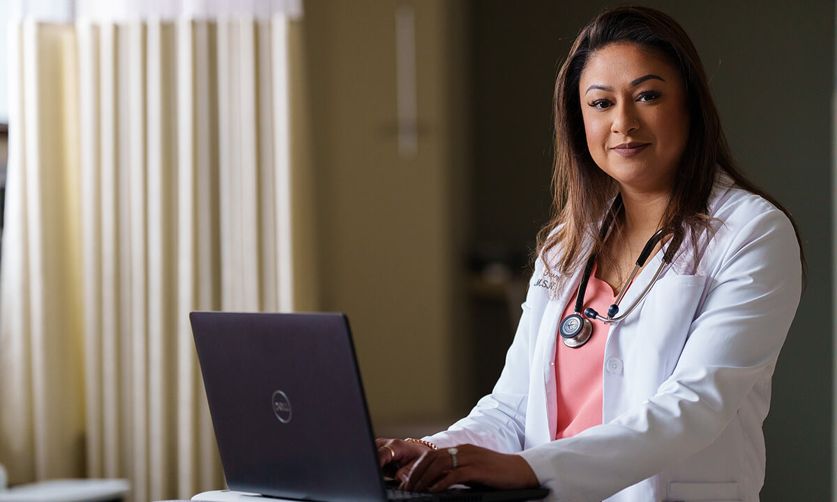 A woman in a medical coat sits before a laptop.