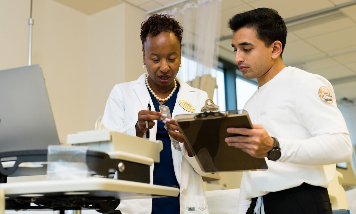 Two people on medical clothing look at a clipboard.