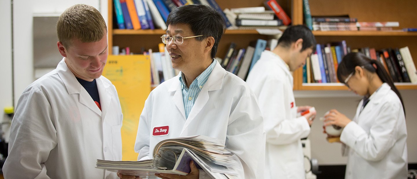 Four people in white lab coats in front of a shelf of books.