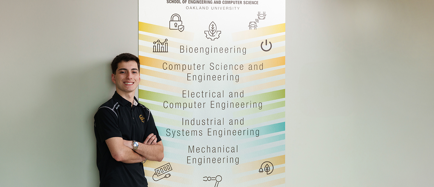 A student standing by a sign that says 