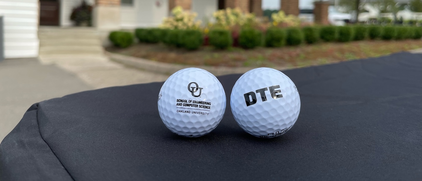 Two golf balls sitting on a table, one with a DTE logo and one with an OU logo