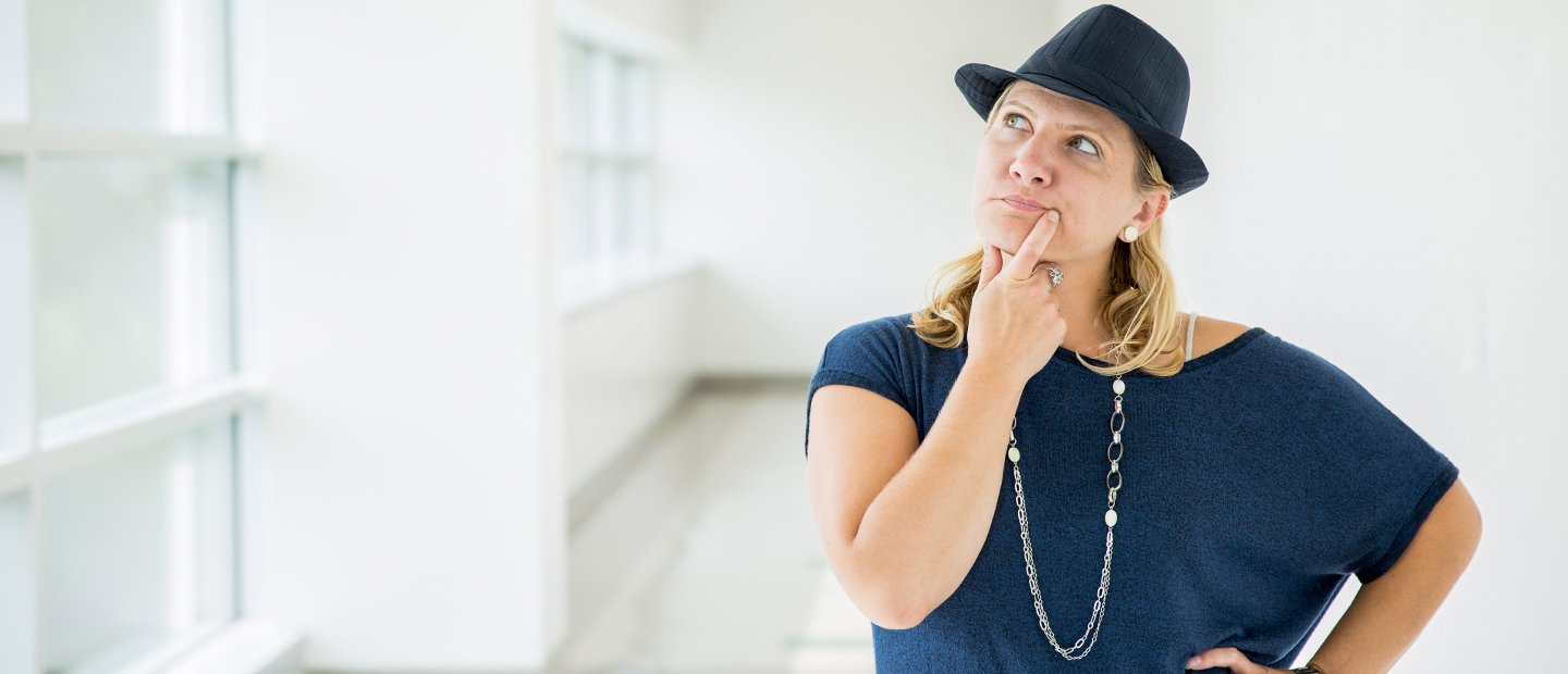 woman in a blue shirt and hat with her hand on her chin and an inquisitive look on her face