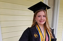 image of Annie Fuelle standing on a porch in her graduation cap and gown