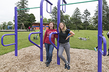 Two women leaning against park equipment at a park with swings and bikes in the background