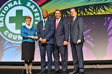 image of four men and one woman in professional attire standing on a stage with a sign in the background reading National Safety Council