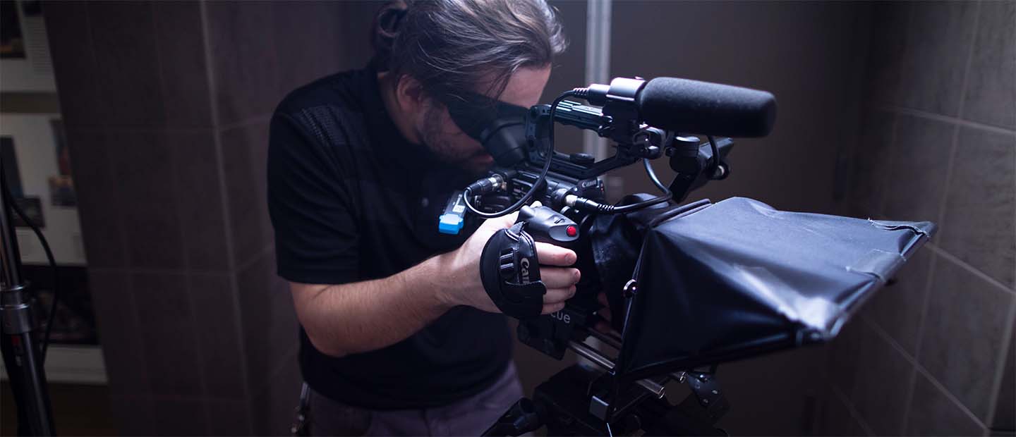 A man standing behind a video camera, filming.