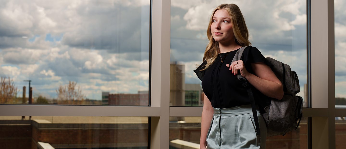 An Oakland University student posing with her backpack in front of a window