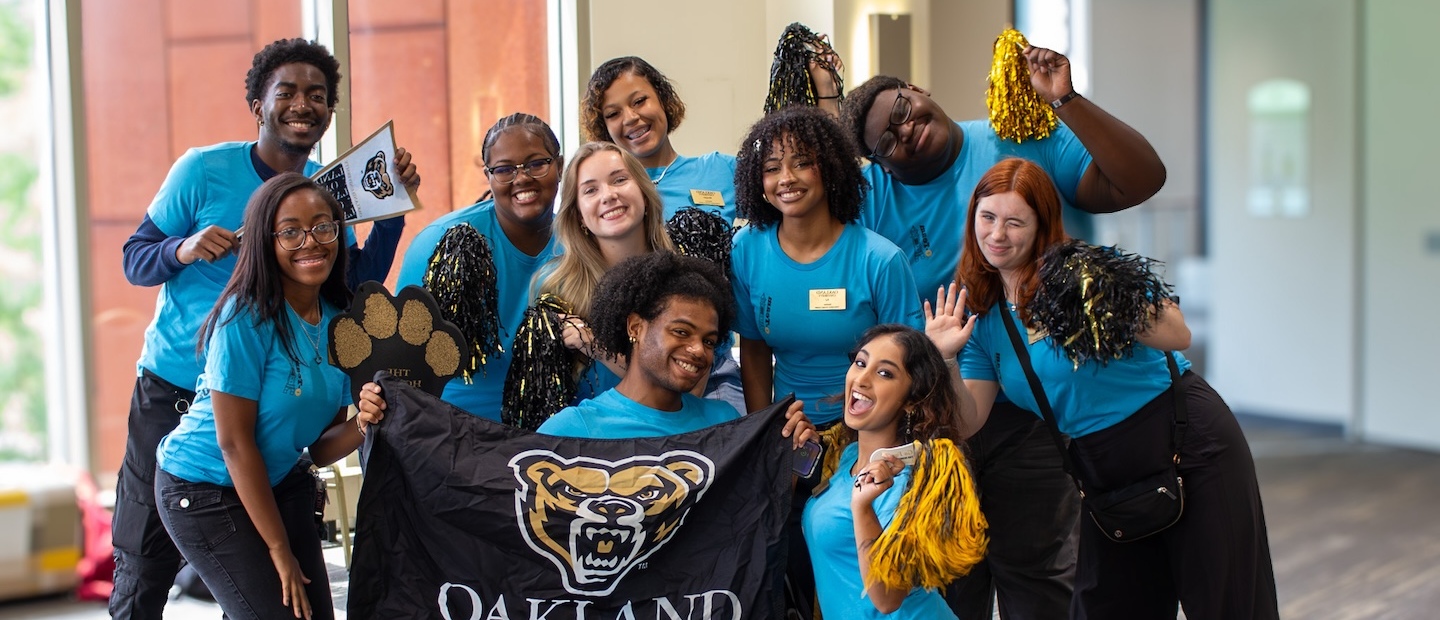 A group of spirited students at orientation, holding an Oakland University banner